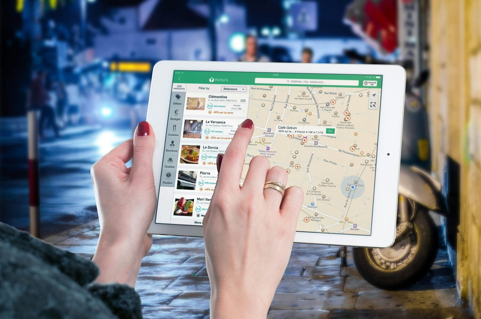 Hands using a digital map on a tablet in an urban setting at night, illustrating navigation and technology.